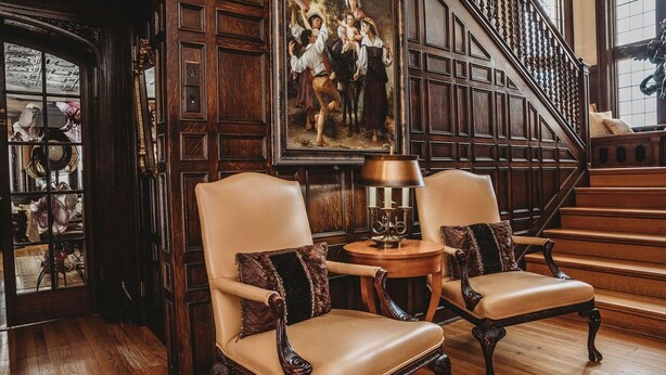Una stanza con due poltrone in pelle, una scala in legno e un quadro appeso al muro.