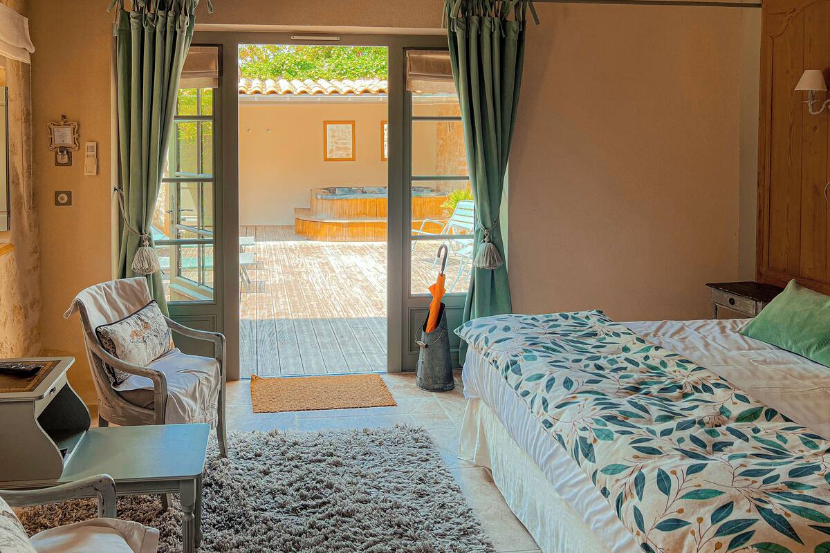 A bedroom with a bed, a chair, a desk, and a view of an outdoor area with a hot tub.