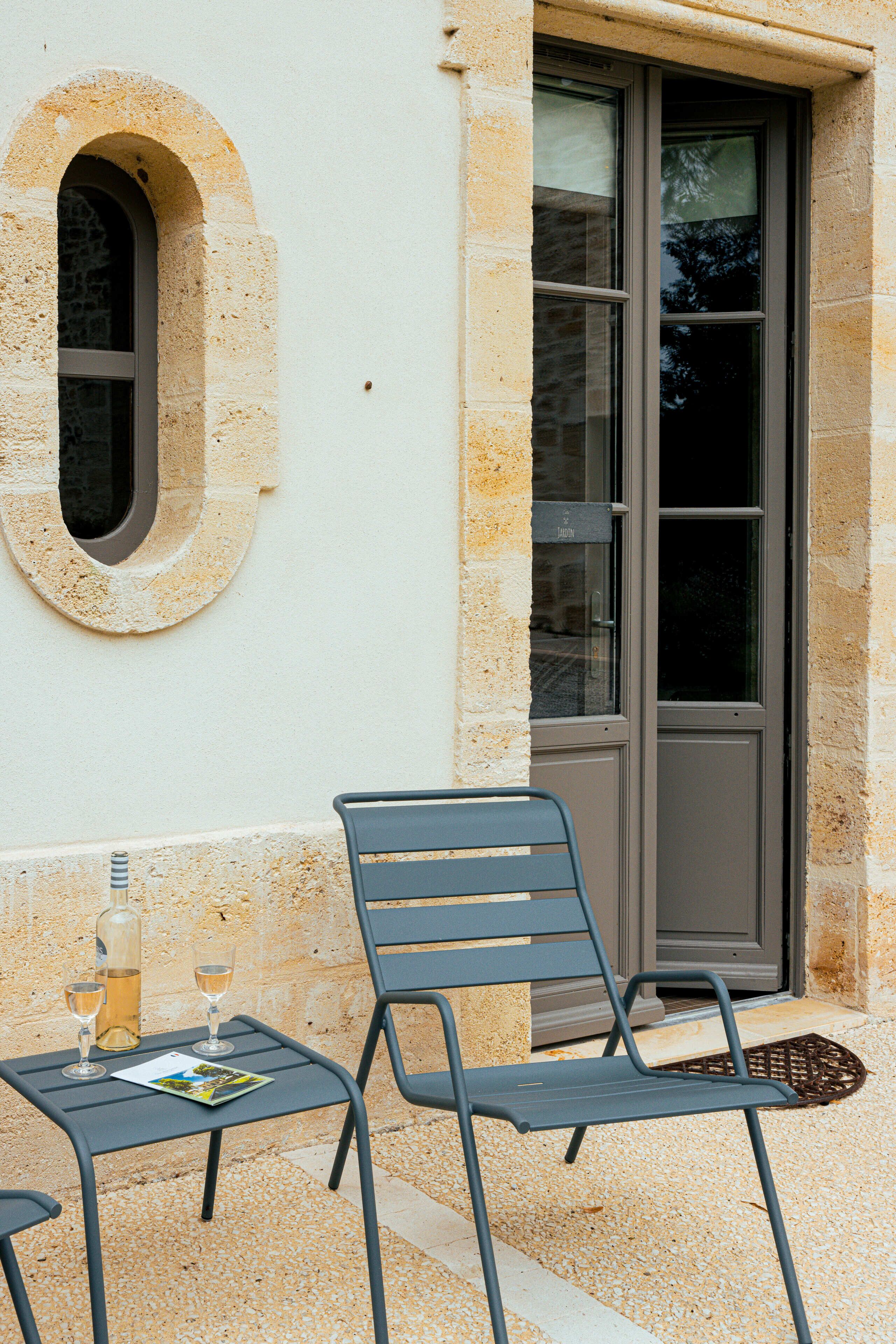 Un bâtiment en pierre avec une fenêtre et une porte, une table avec deux chaises, et une bouteille et des verres sur la table.
