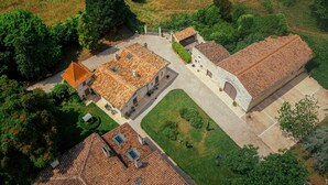 An aerial view of a property with multiple buildings, including a large stone building with a tiled roof, smaller structures with tiled roofs, and surrounding greenery. - Clos Marcamps (Prignac-et-Marcamps)
