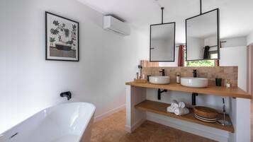 Um banheiro moderno com uma banheira independente, duas pias com espelhos, um porta-toalhas e uma impressão emoldurada de tema botânico na parede.
