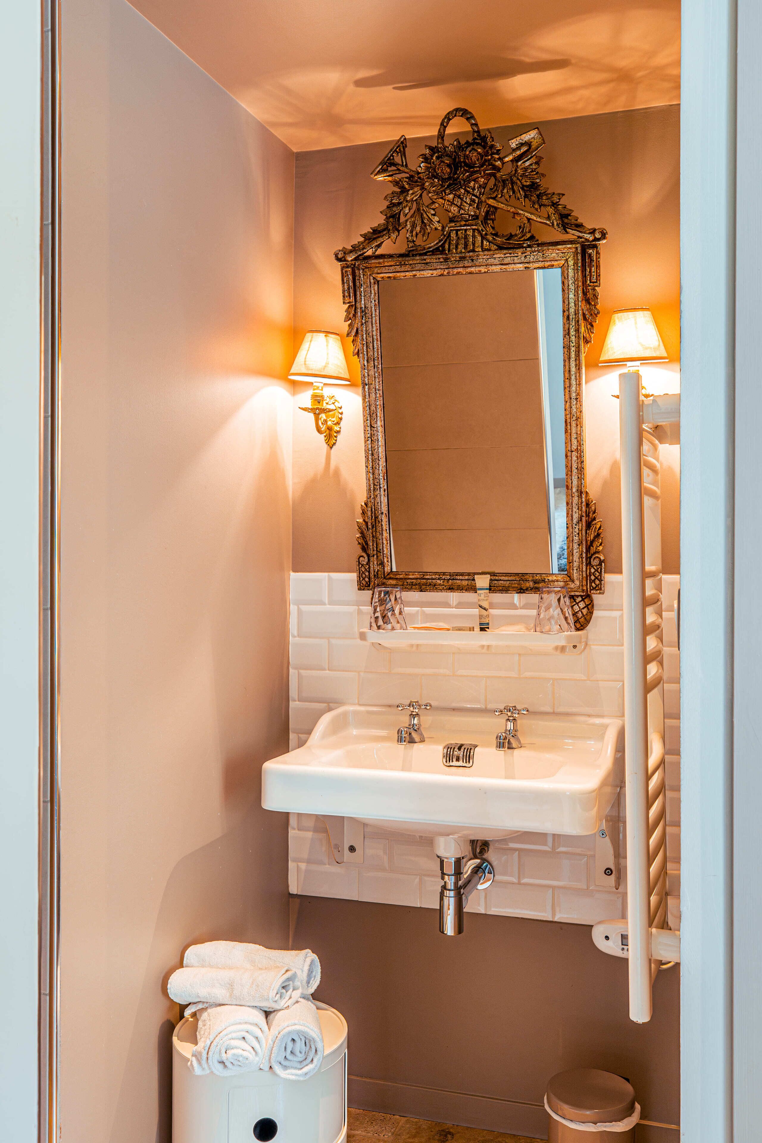 Un baño con lavamanos blanco, espejo decorado y dos lámparas de pared.