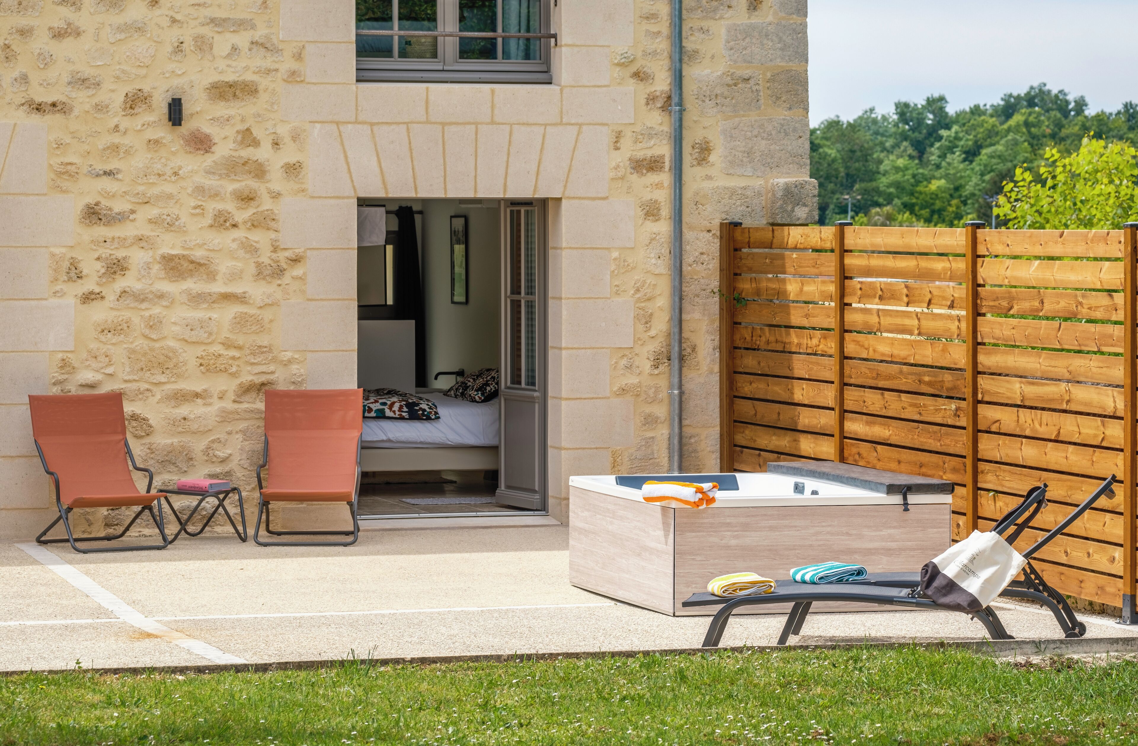 Un bâtiment en pierre avec une clôture en bois, un jacuzzi et deux chaises longues.