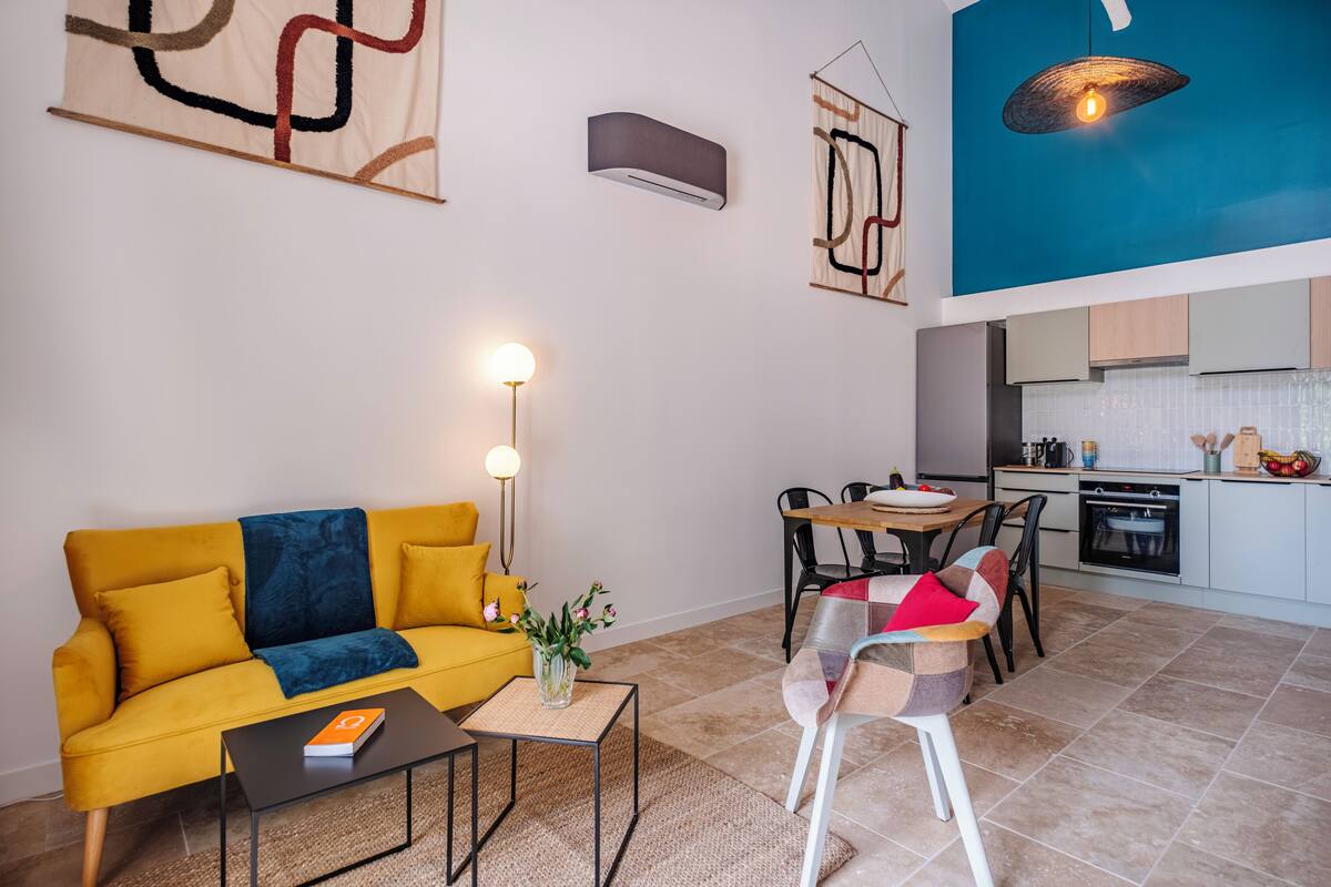 A modern living room with a yellow sofa, a coffee table, and a dining area with a wooden table and chairs.
