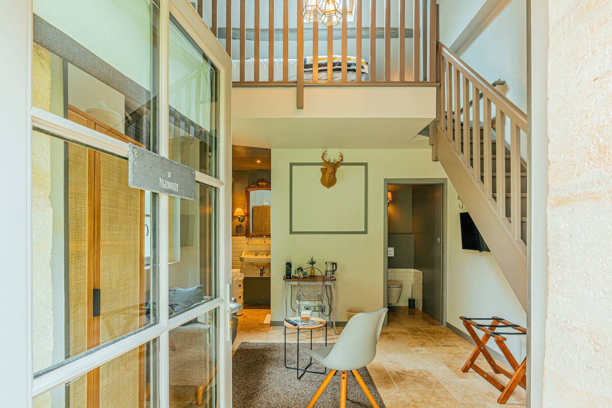 A spacious living area with a high ceiling, a staircase, and a dining area with a table and chairs.