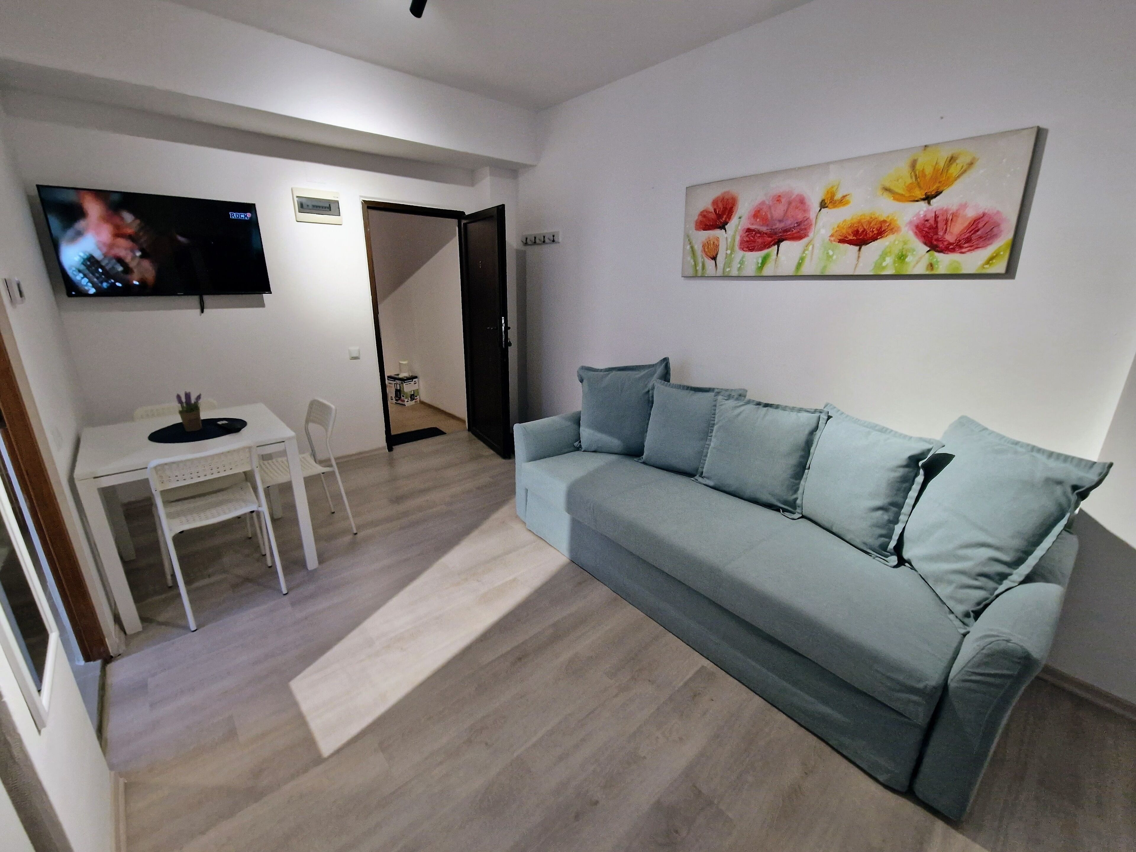 Una sala de estar con un sofá gris, una mesa blanca y un televisor montado en la pared.
