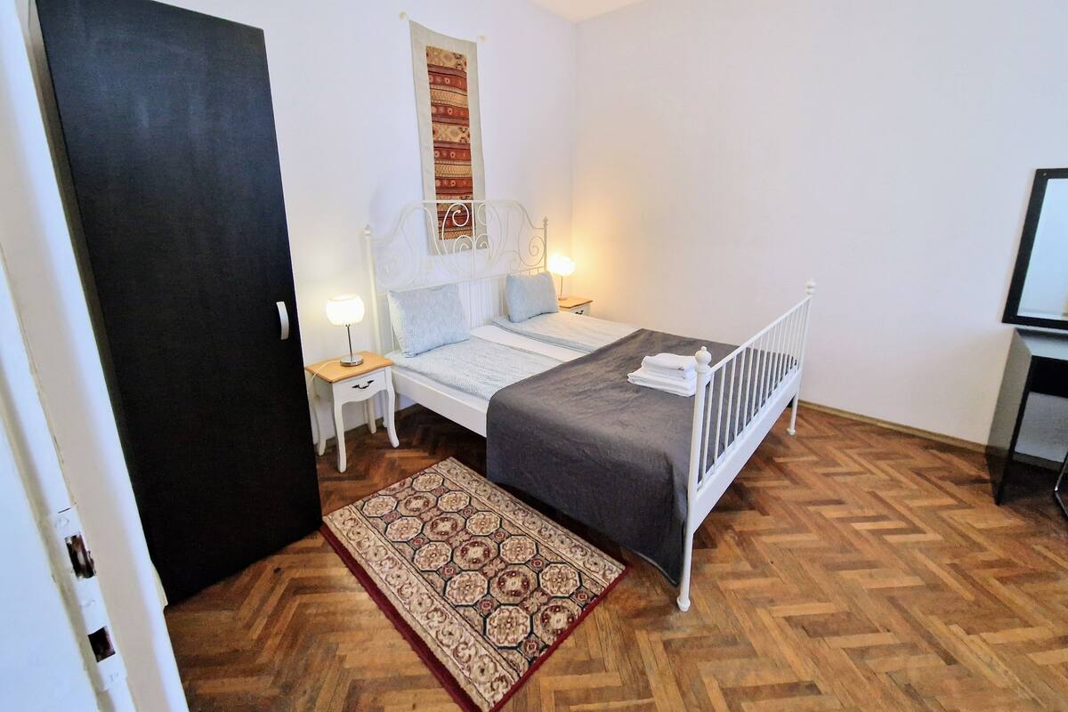A bedroom with a bed, bedside tables, a nightstand, a rug, and a door.
