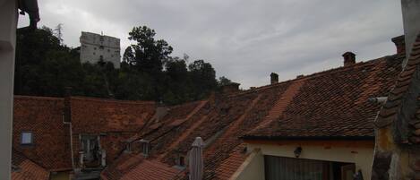 A residential building with a tiled roof, a balcony with a sofa and table, and a view of a castle in the background.