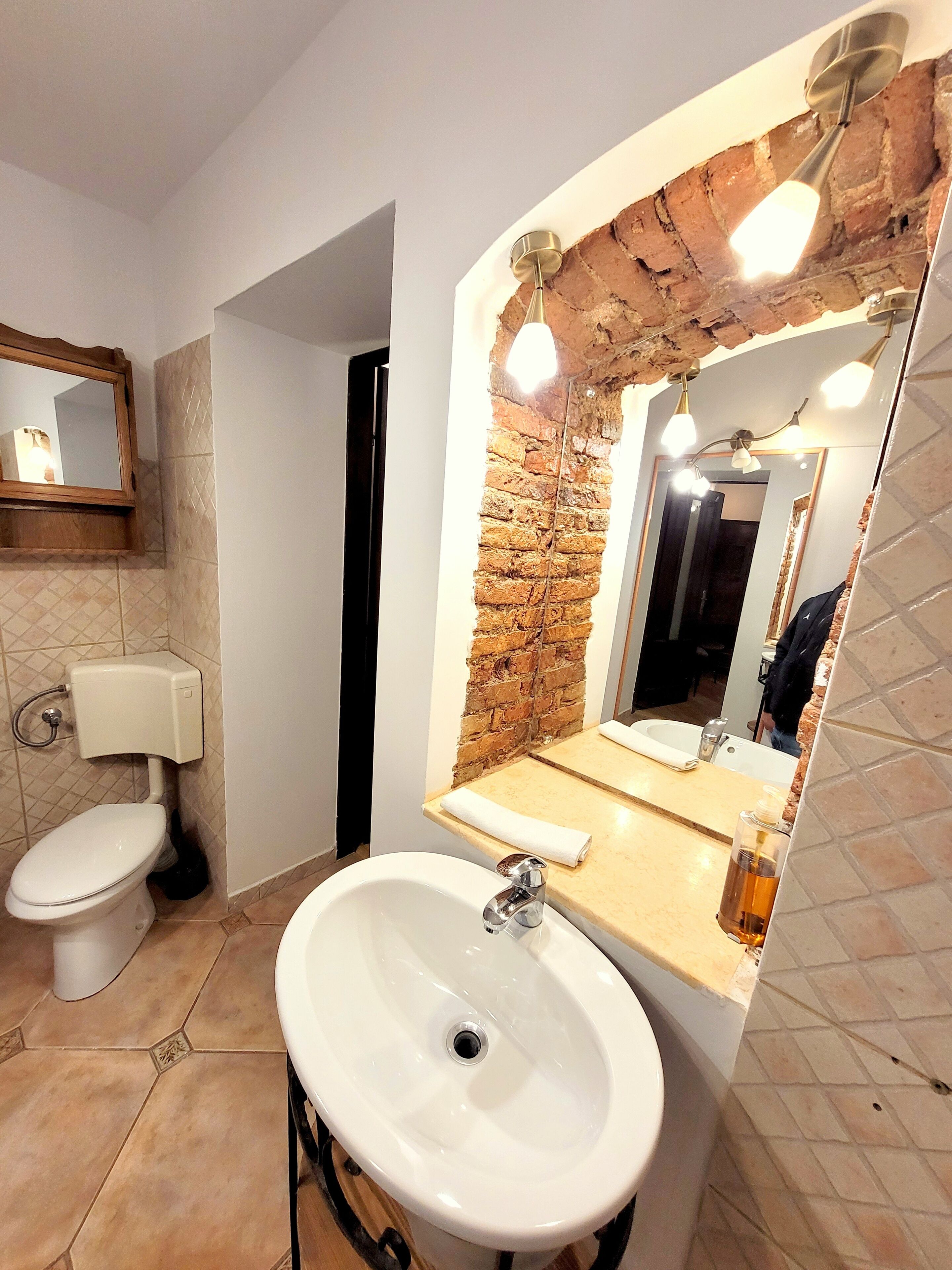 A bathroom with a white toilet, a sink with a mirror above it, and a brick wall.