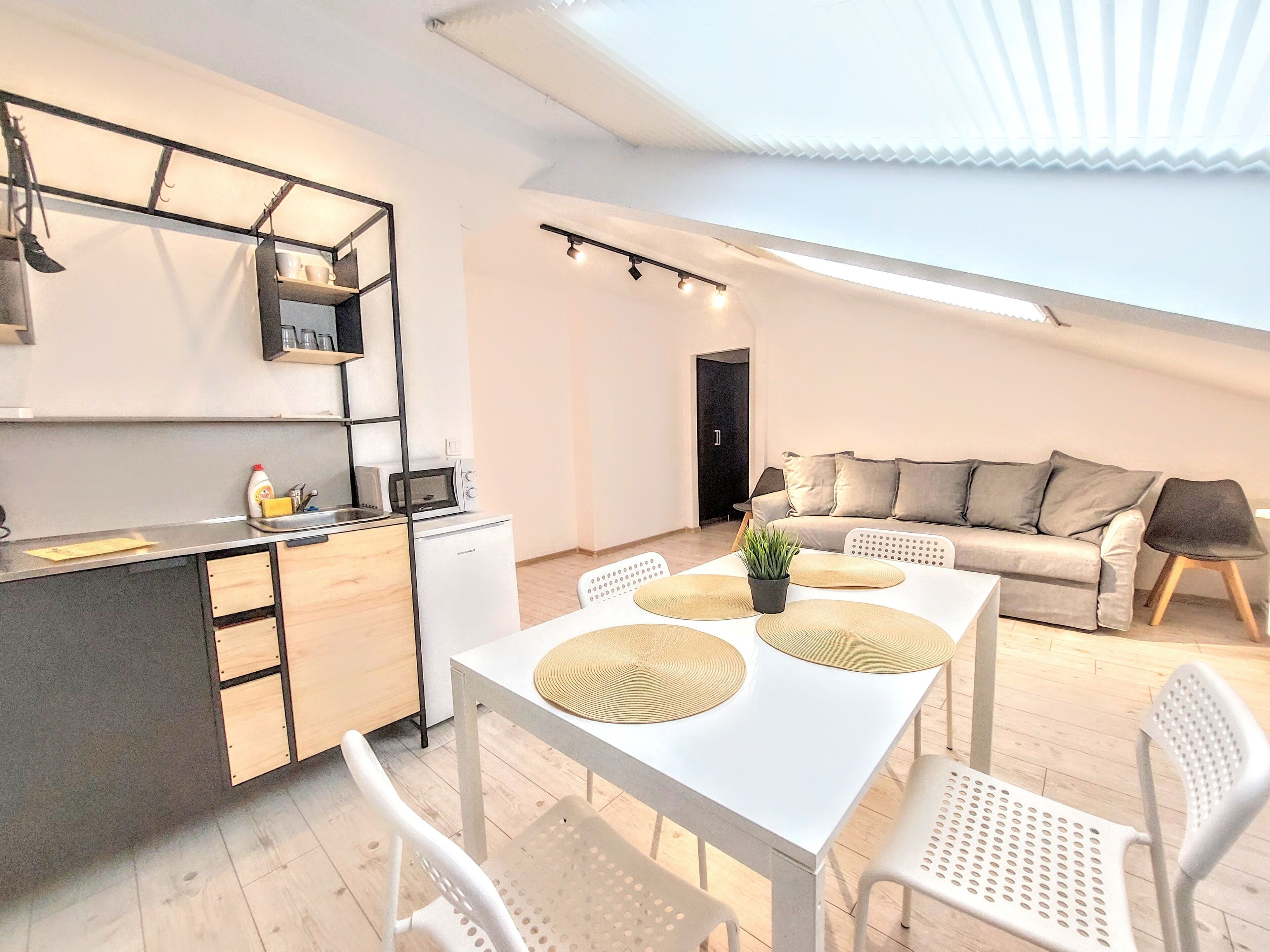 A modern kitchen with a dining area, a sofa, and a small refrigerator.