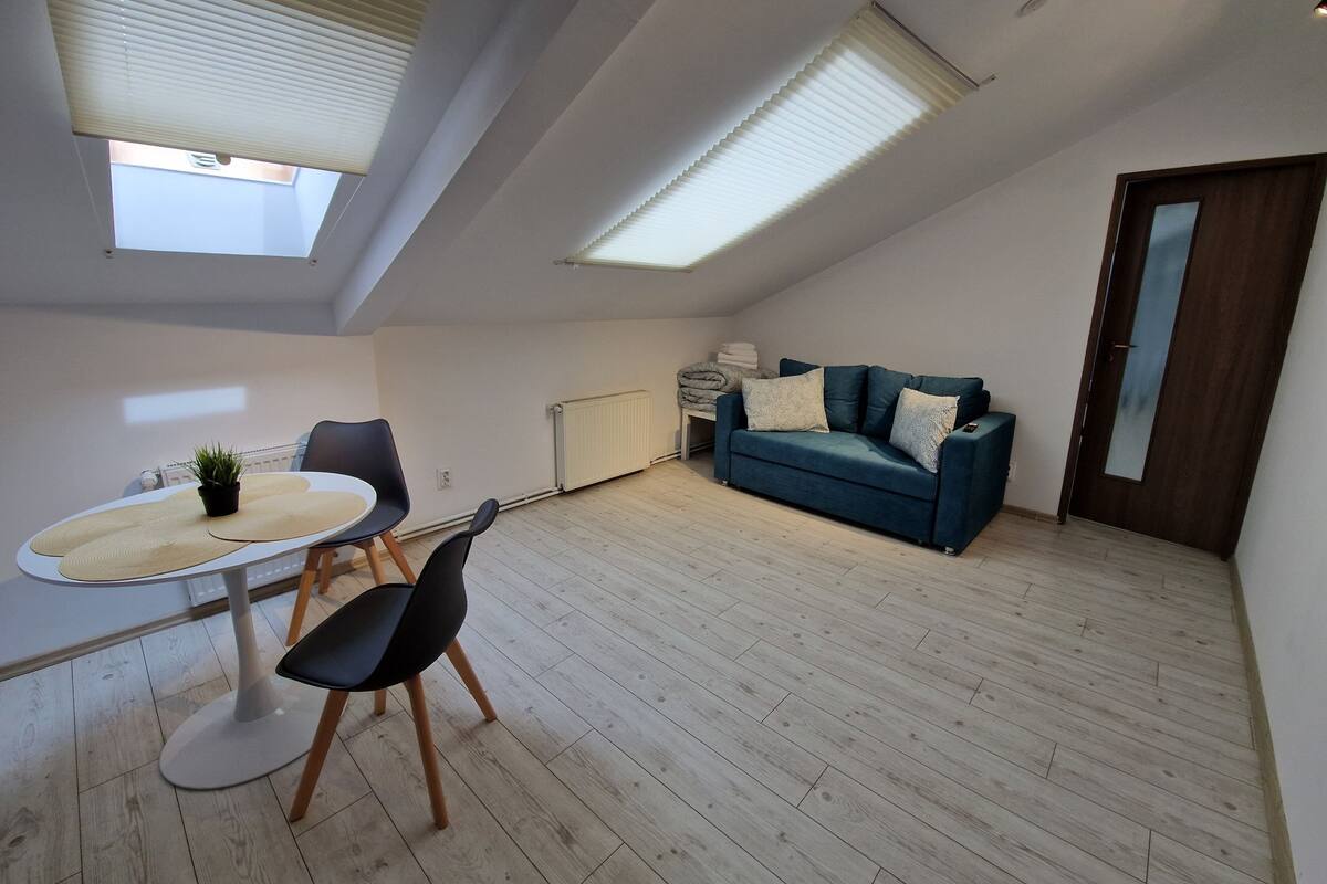 A modern loft apartment with a dining area, a sofa, and a large window.