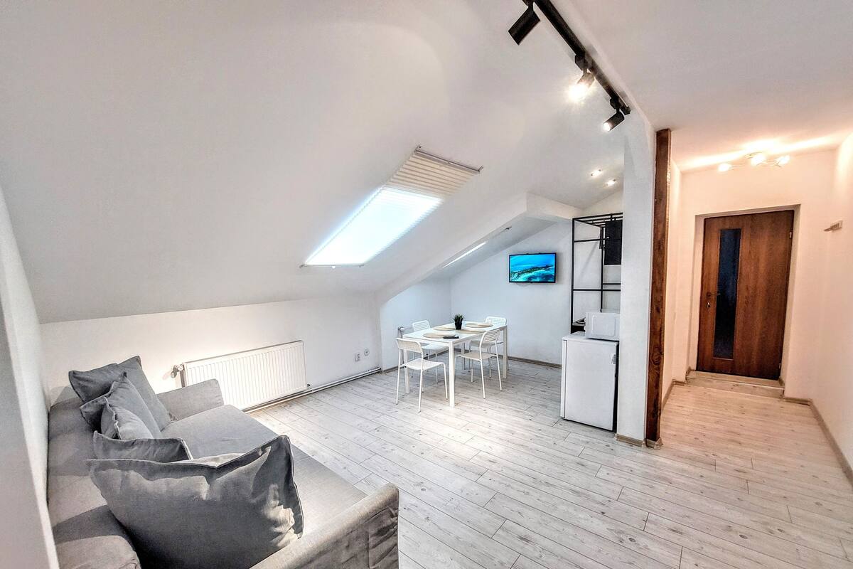A modern loft apartment with a dining area, kitchenette, and a large window.