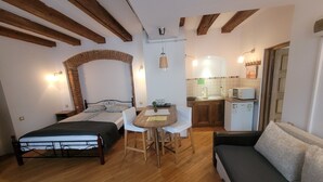 A compact room with a bed, a sofa, a dining table with chairs, a small kitchen area with a microwave, and a brick wall. - Main Square Apartments & More (Brasov)
