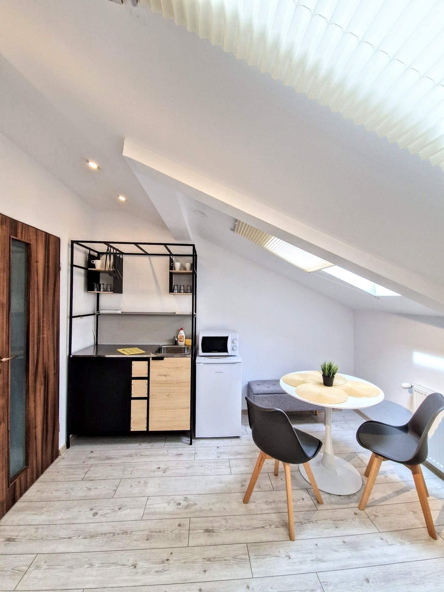 A modern kitchen with a built-in oven and microwave, a dining area with two chairs and a small table, and a wooden floor.