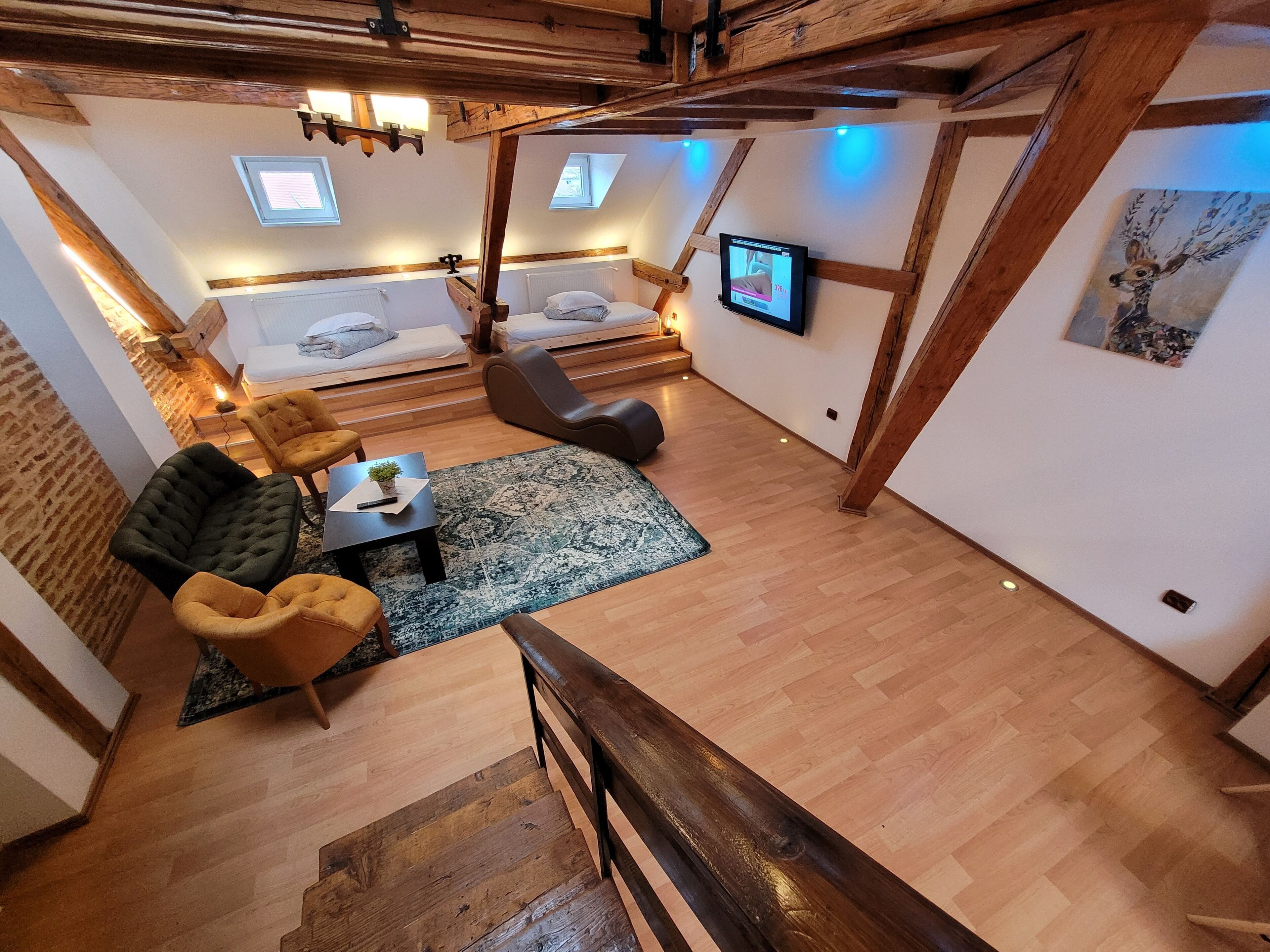 Een kamer in loftstijl met zichtbare houten balken, een bed, een bank, een televisie en een schilderij.