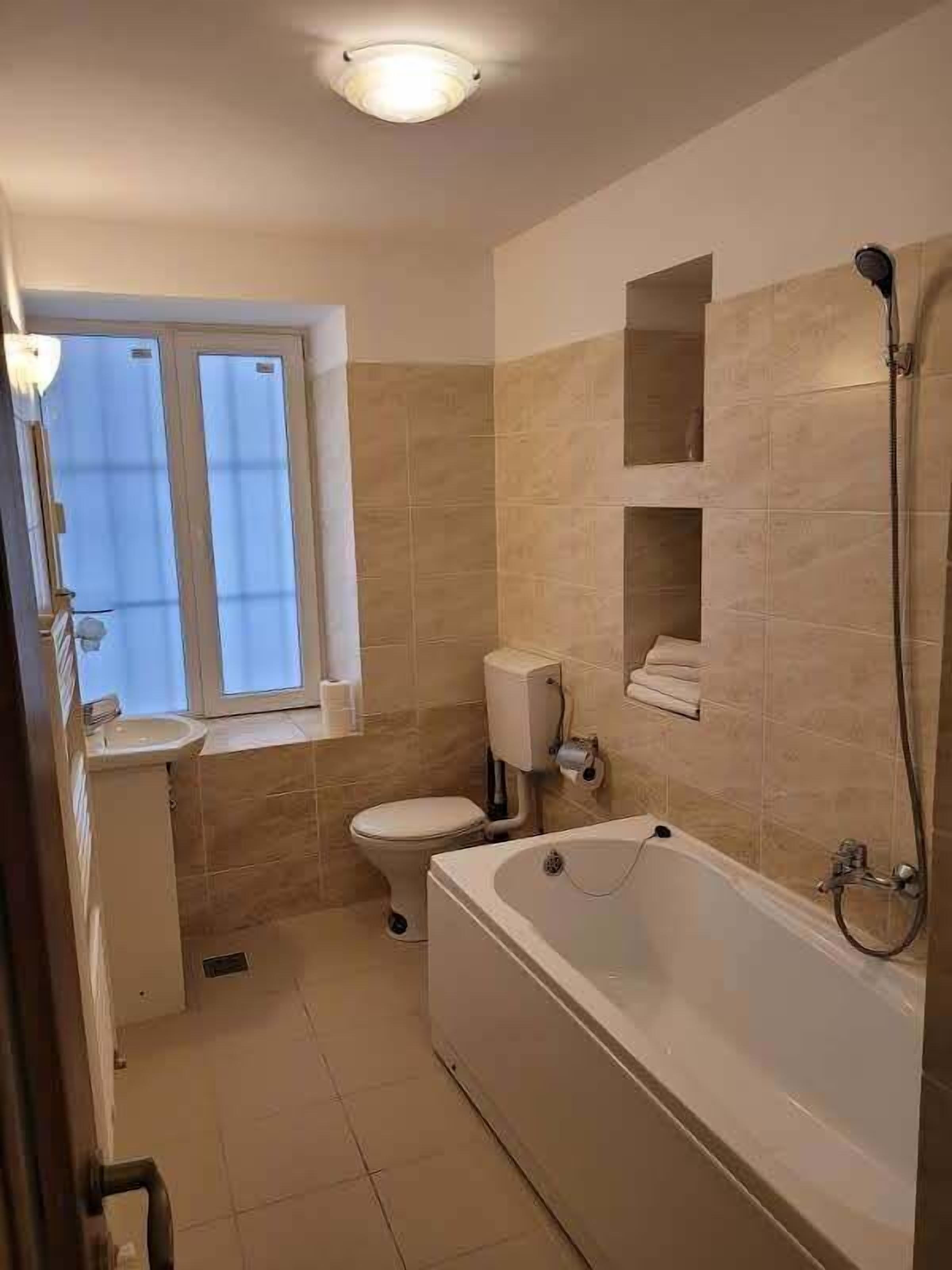 A bathroom with a bathtub, toilet, and sink. There is a window providing natural light.