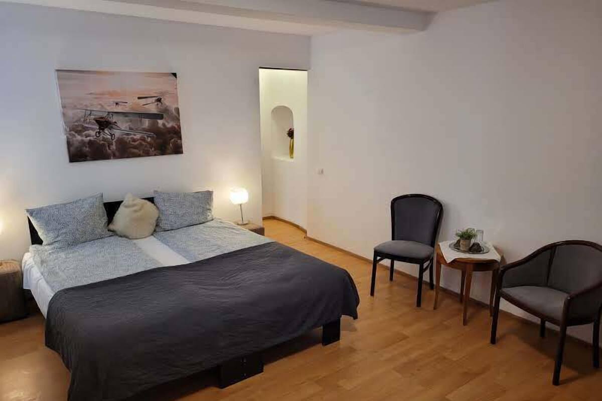 A bedroom with a bed, two chairs, a small table, and a wall-mounted picture.