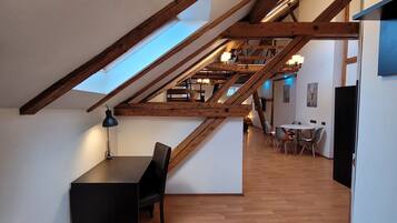 A spacious loft with a sloped ceiling, wooden beams, a skylight, a dining area with chairs, and a black table.