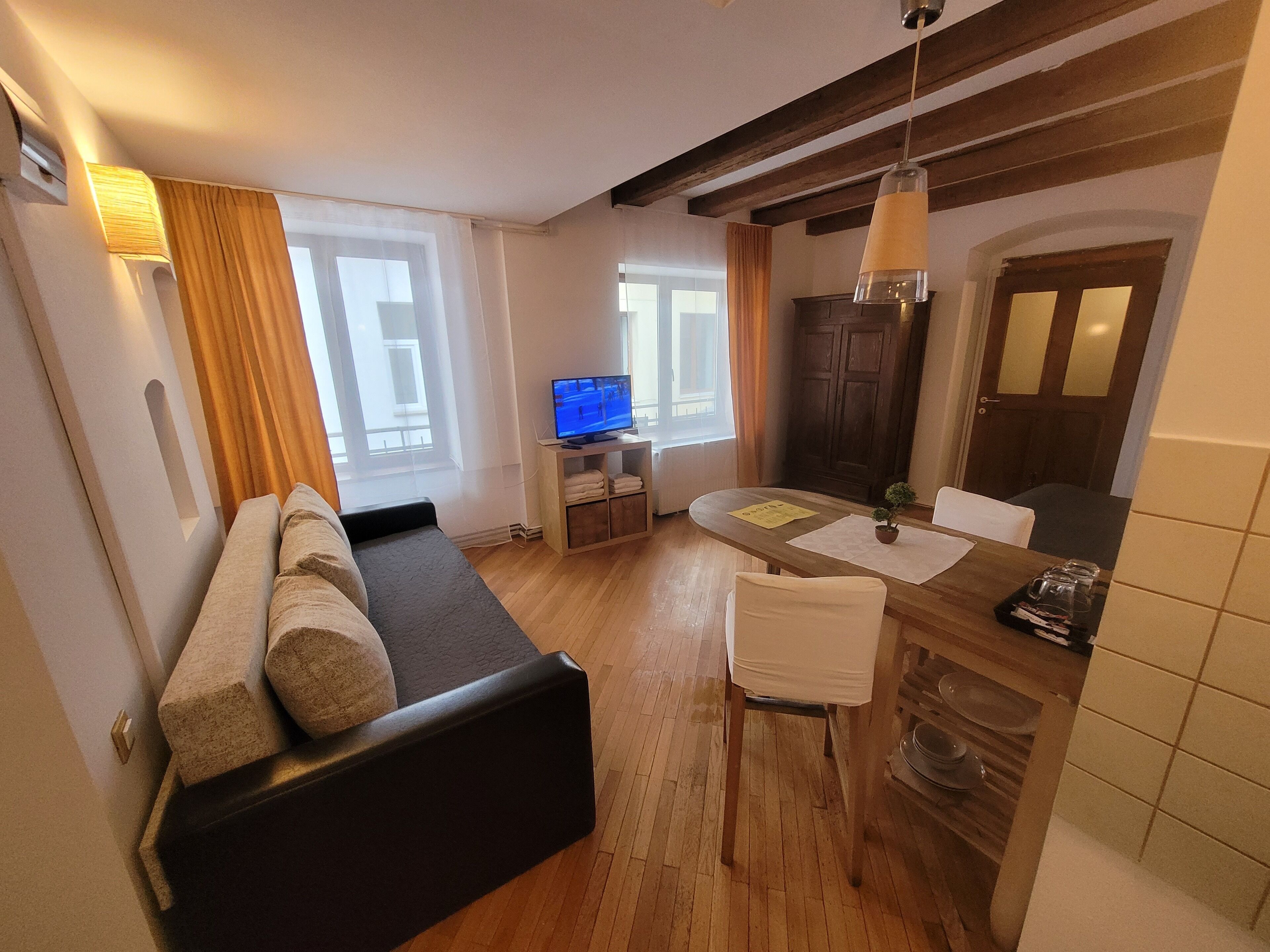 A compact living space with a sofa, a dining table with chairs, a television, and a small kitchen area.