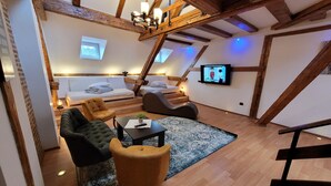 A cozy loft-style room with a loft bed, a sofa, a chair, a small table, and a TV. - Main Square Apartments & More (Brasov)