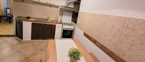 A compact kitchen with a gas stove, a sink, and a small countertop. There is a wooden table with a potted plant in the center.