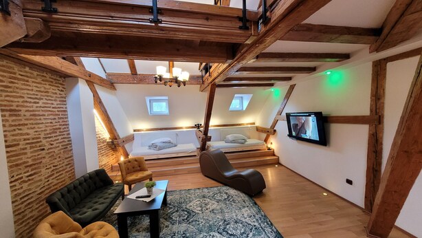 A loft-style room with exposed wooden beams, a loft bed, a sofa, a coffee table, and a television. - Main Square Apartments & More (Brasov)