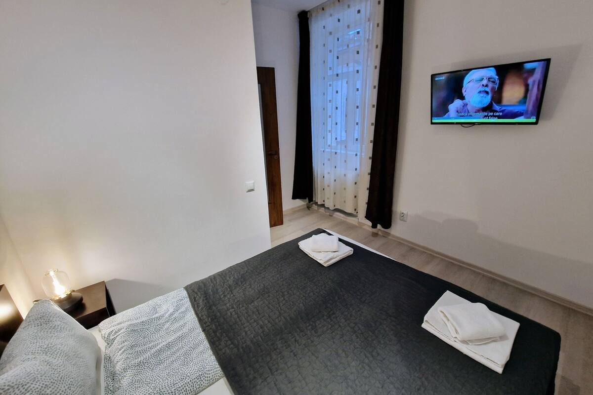 A hotel room with a bed, a TV on the wall, and a window with curtains.