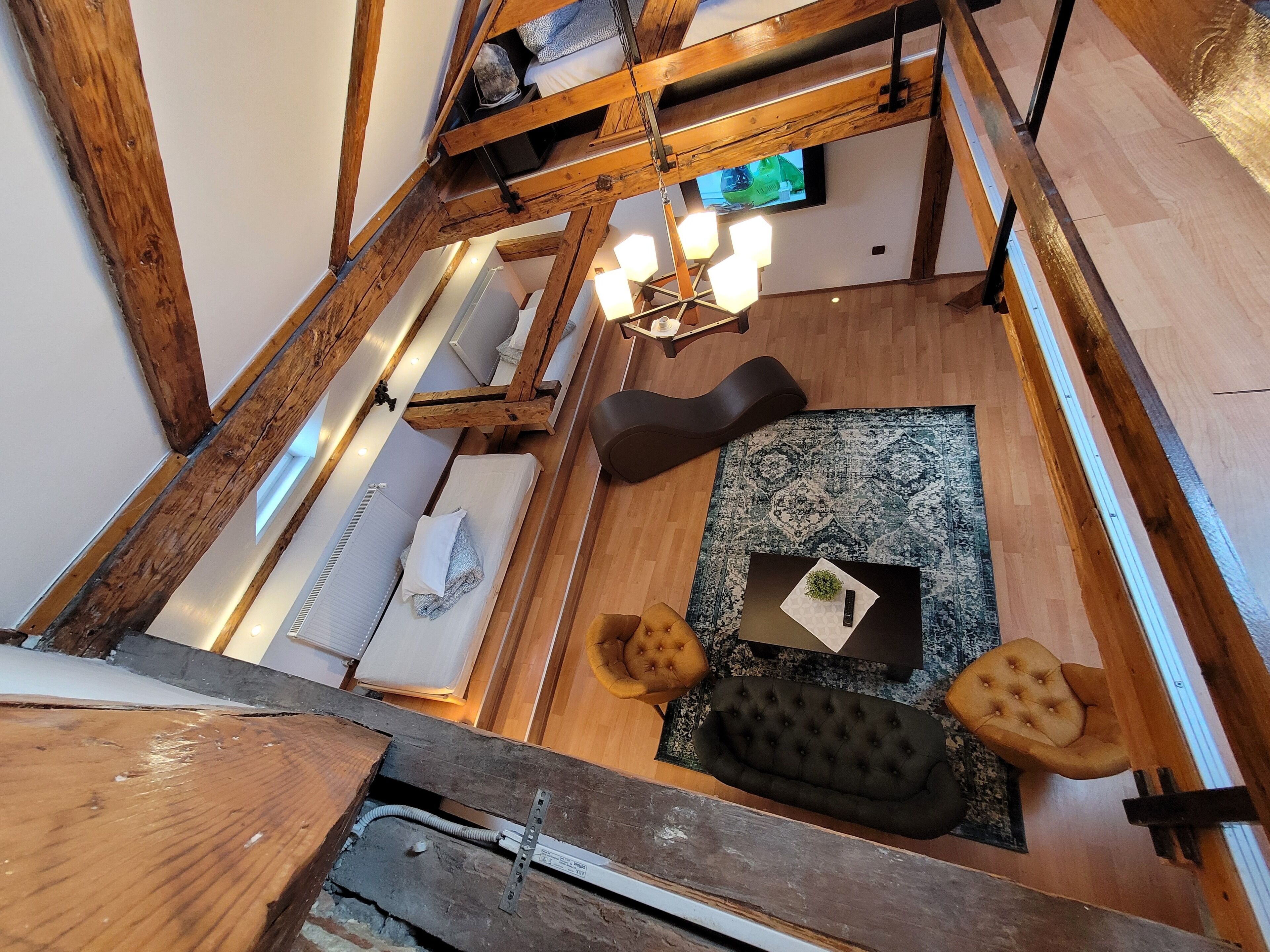 Un cuarto estilo loft con vigas de madera a la vista, un sofá negro, una alfombra pequeña y un televisor montado en la pared.