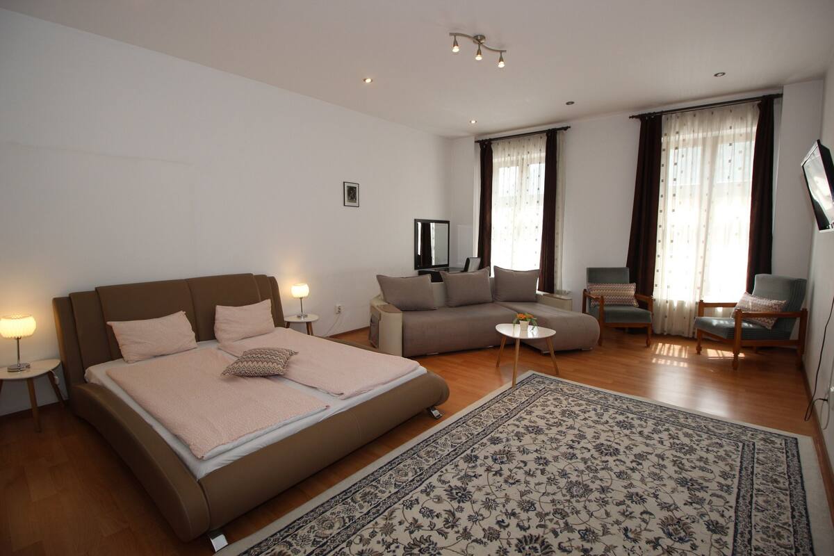 A modern hotel room with a large bed, a sofa, a TV, and a small table.