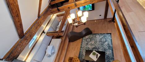 A loft-style room with exposed wooden beams, a black sofa, a patterned rug, and a small table with a remote control.