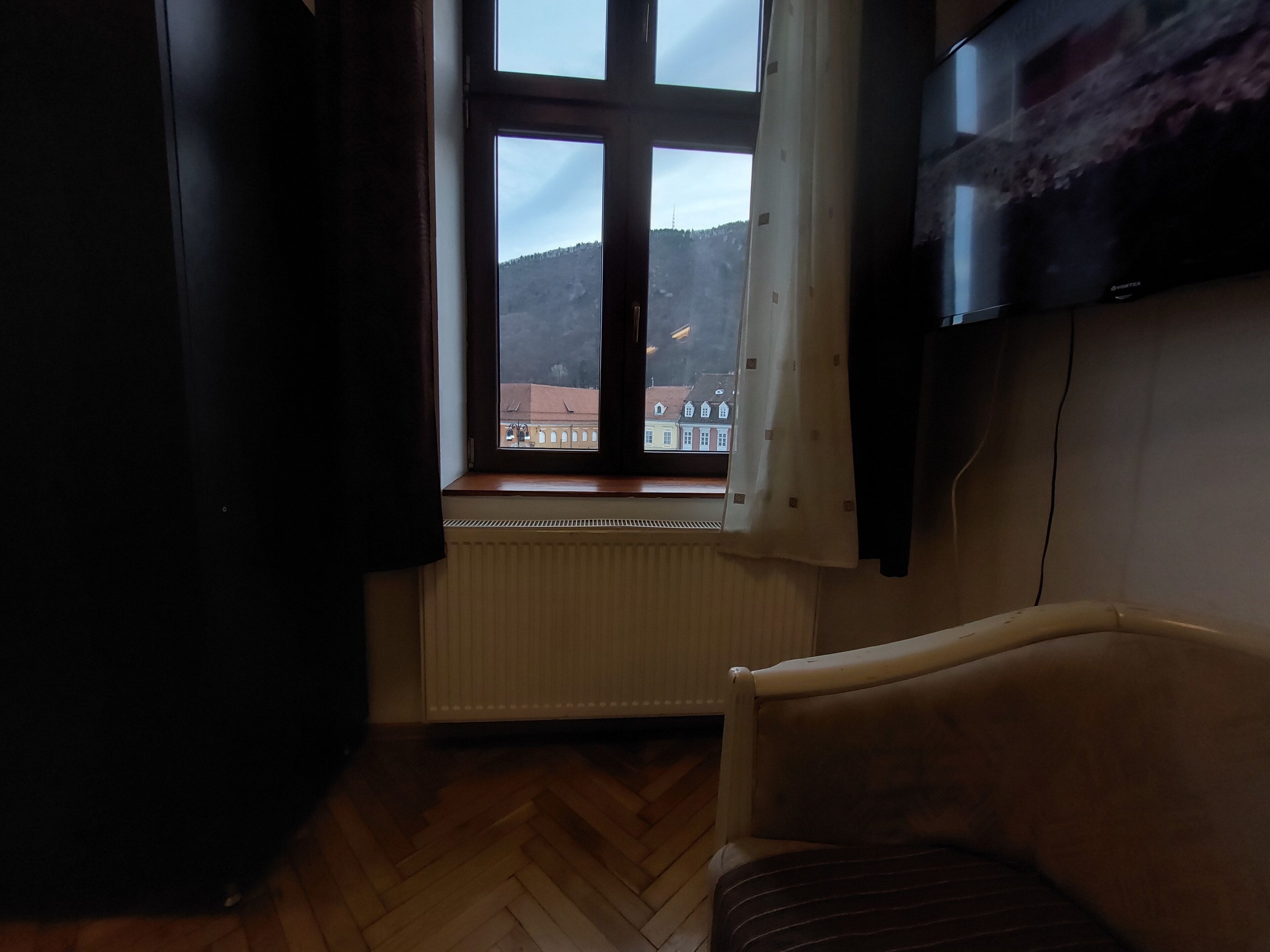 Una habitación con un ventanal grande, un radiador, un televisor en la pared y una silla.