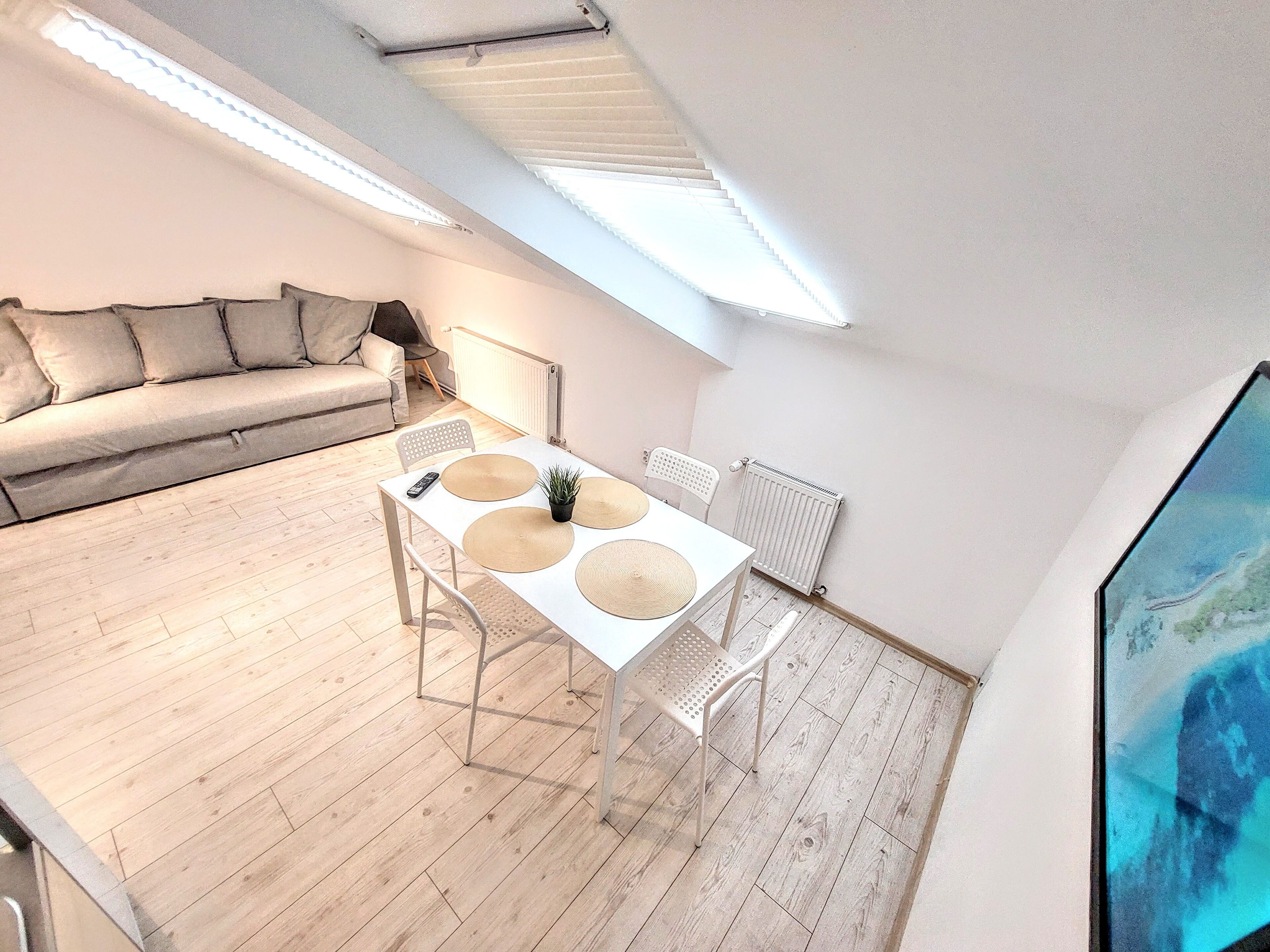 A modern loft apartment with a dining area, a sofa, and a large window providing natural light.