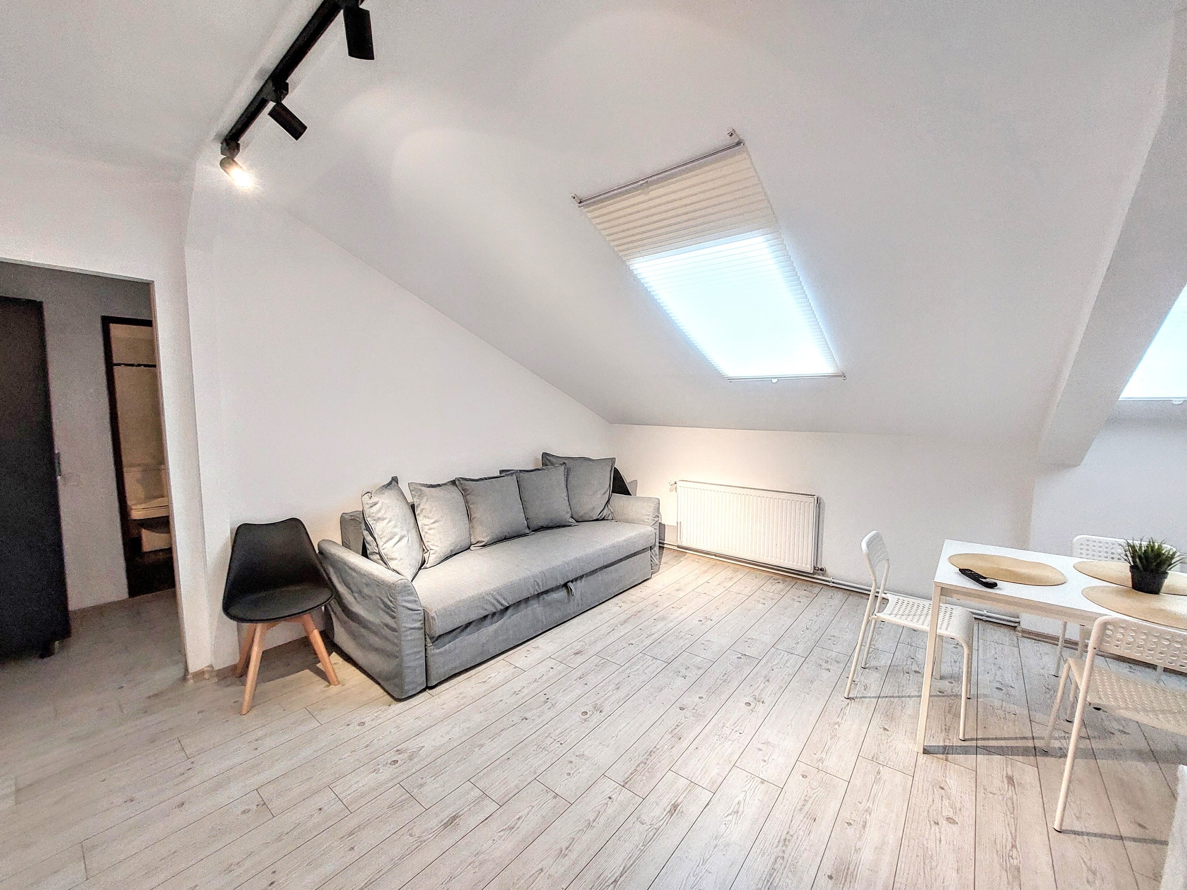 A modern loft apartment with a grey sofa, a dining table with chairs, and a skylight.