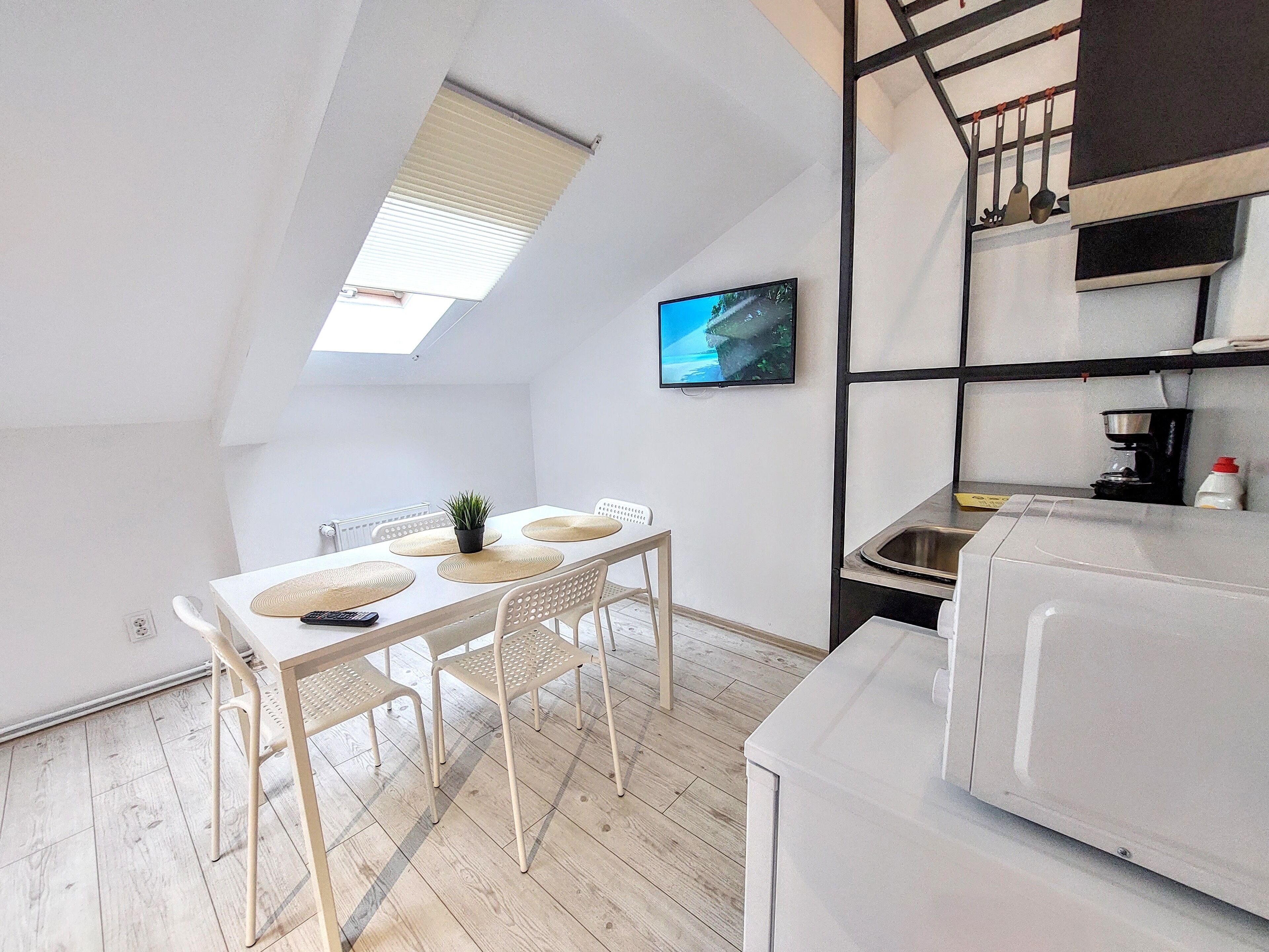 Eine kleine, moderne Küche mit Essbereich, einem an der Wand befestigten Fernseher und einer Treppe, die zu einer oberen Ebene führt.