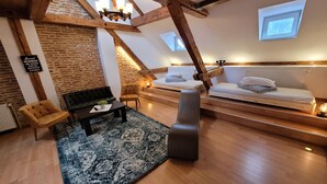 A loft-style room with exposed wooden beams, a brick wall, a chandelier, a sofa, a chair, a small table, a bench, and a bed. - Main Square Apartments & More (Brasov)