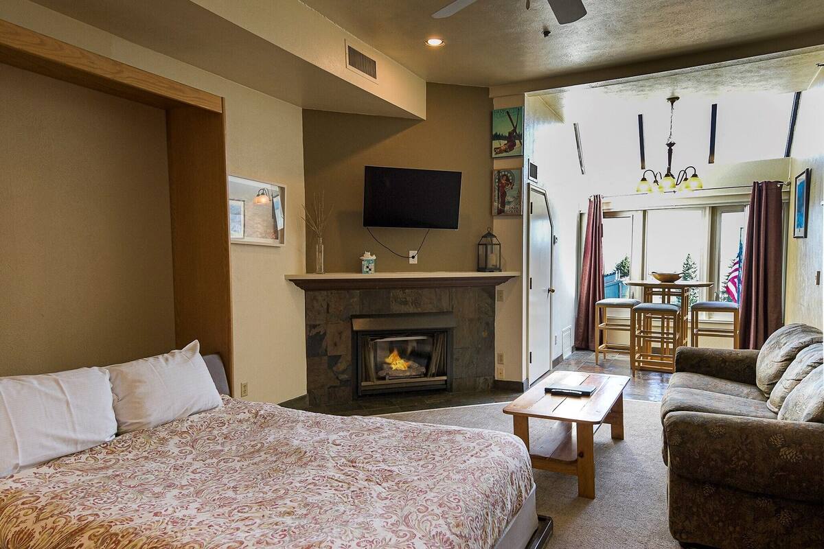 A bedroom with a large bed, a fireplace, a TV, and a dining area with chairs and a table.
