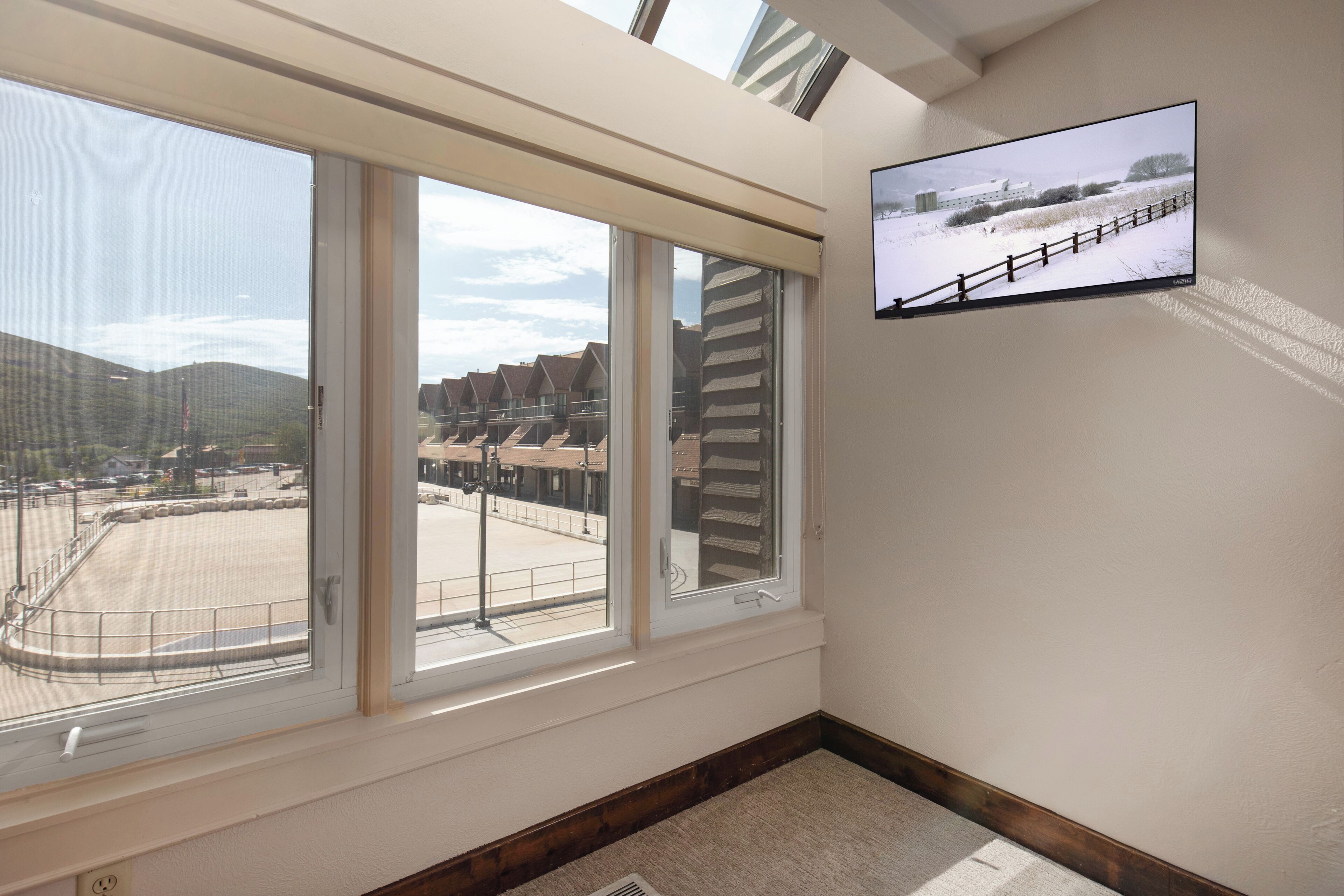 Ein Zimmer mit großem Fenster mit Blick auf einen Parkplatz und ein Gebäude mit geneigtem Dach.