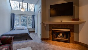 A bedroom with a bed, a fireplace, a TV mounted above it, and a window with curtains. - Lodge at Mountain Village by Park City Vacations (Park City)
