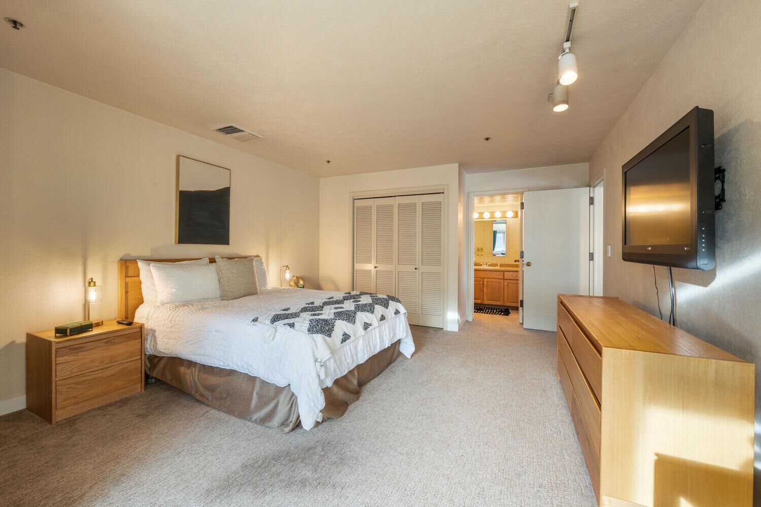 Une chambre à coucher comprenant un lit, des tables de chevet, un téléviseur et un dressing.