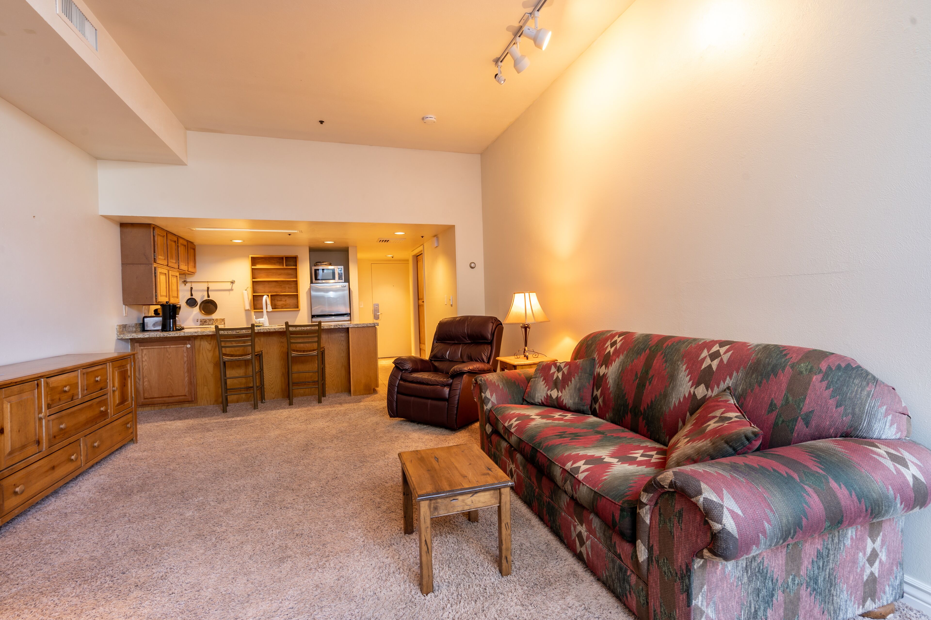 A living room with a sofa, a wooden table, and a kitchen area in the background.