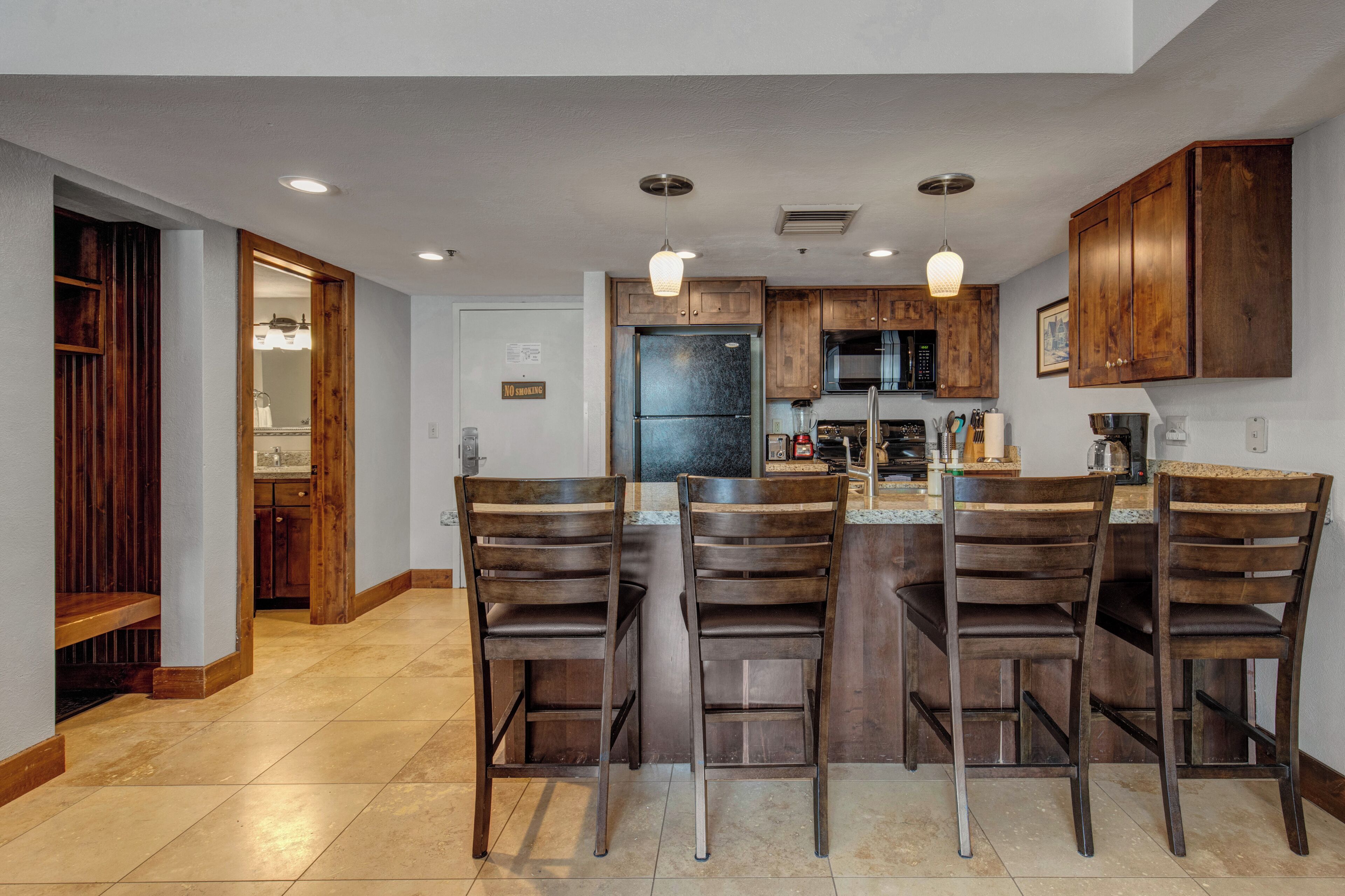A modern kitchen with a central island, bar stools, wooden cabinets, and a microwave.