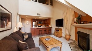 A spacious living area with a high ceiling, a kitchen with a bar, a fireplace, and a television mounted on the wall. - Lodge at Mountain Village by Park City Vacations (Park City)