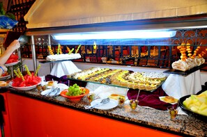 A buffet with various food items and a person serving. - Royal Lido Resort & Spa (Dar Chaabane Al Fehri)