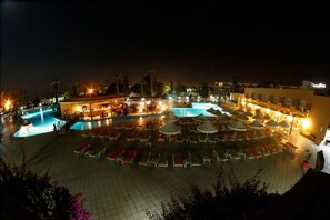 A nighttime view of a resort with multiple swimming pools, outdoor seating areas, and a bar/lounge area. - Royal Lido Resort & Spa (Dar Chaabane Al Fehri)