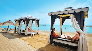 Een strand met twee zonnedaken, waarvan één met een persoon die uitrust en de ander met twee zittende personen.