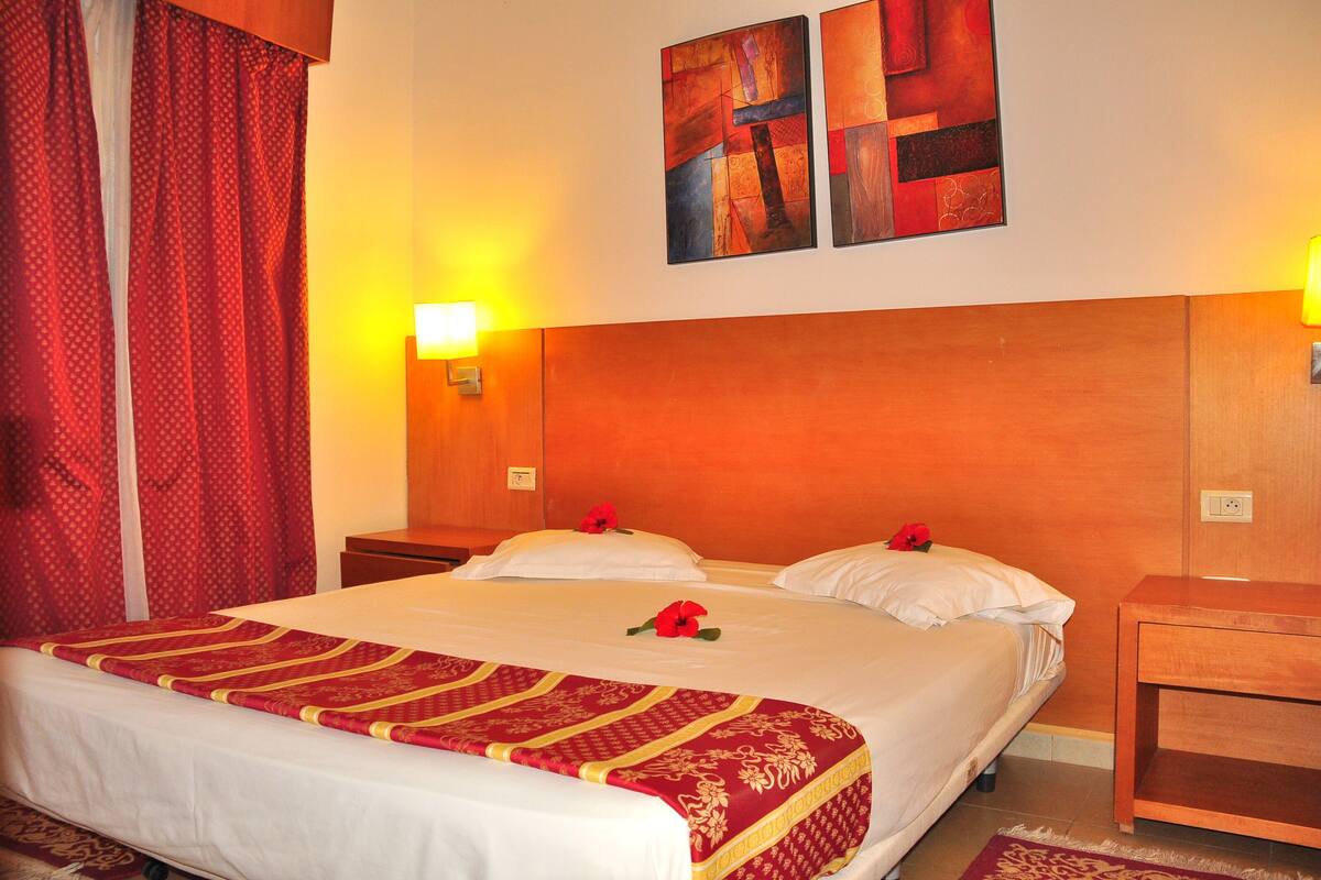 A hotel room with a large bed, two bedside tables, and a red curtain.