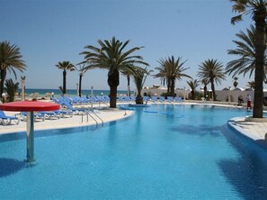 A pool area with blue water, surrounded by palm trees and blue lounge chairs. - Royal Lido Resort & Spa (Dar Chaabane Al Fehri)