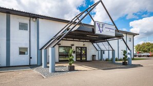 A hotel entrance with a covered walkway, a sign reading "Peterborough by Vervhotels," and a parking lot in the background. - Peterborough by Verve (Peterborough)