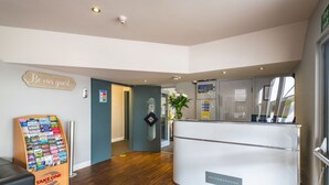 A reception area with a 'Take One' brochure stand, a 'Be our guest' sign, a reception desk labeled 'Peterborough', and a 'No Smoking' sign. - Peterborough by Verve (Peterborough)