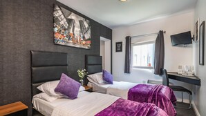 A hotel room with two beds, a desk, a chair, a TV, and a window with curtains. - Peterborough by Verve (Peterborough)